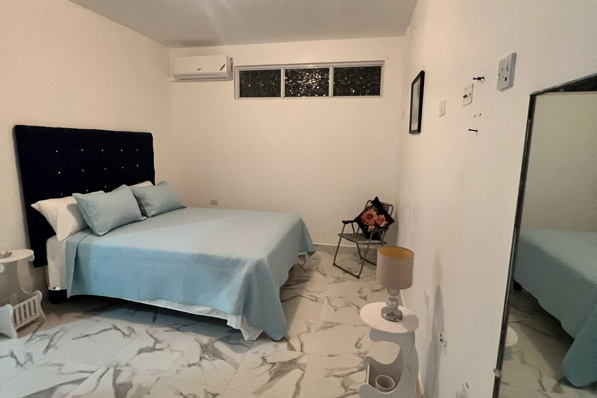Un dormitorio con cama, una silla, una lámpara, una ventana y un espejo.