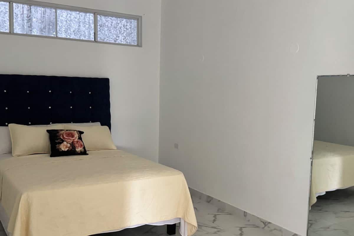 Un dormitorio con cama, cabecero, ventana y espejo.