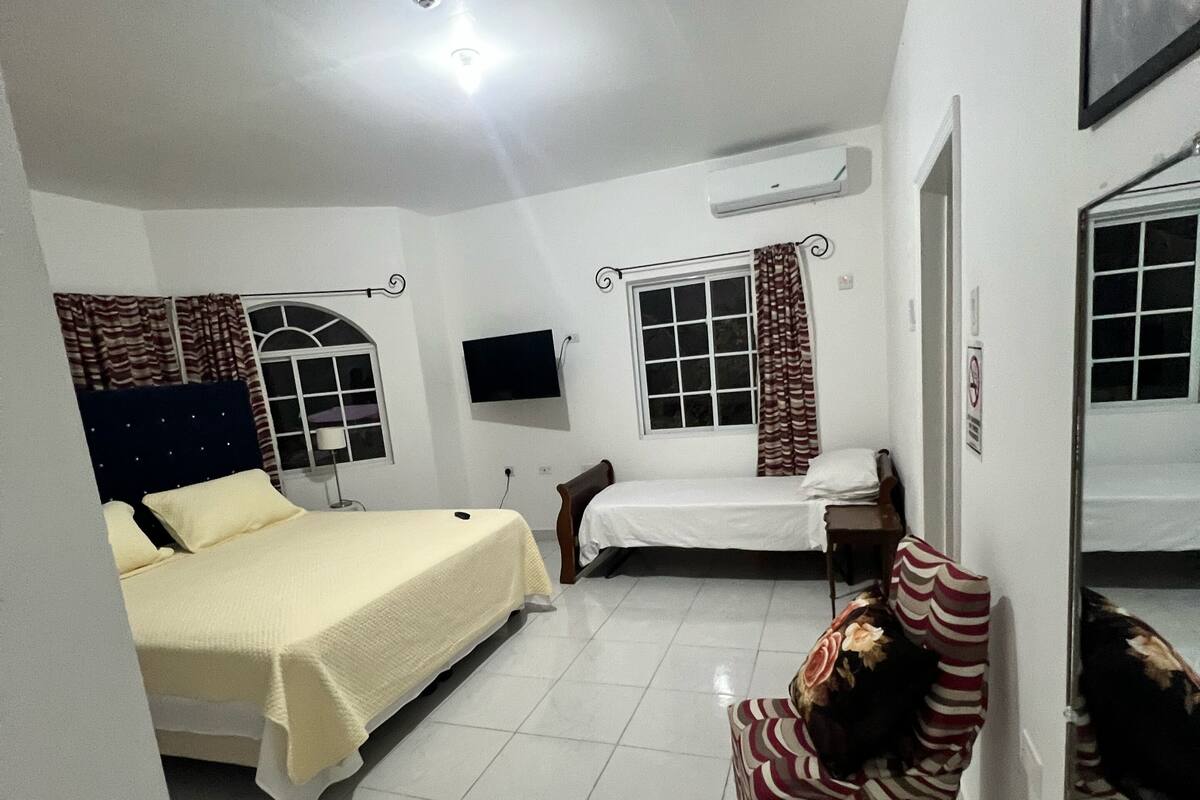 Habitación de hotel con dos camas, televisión, una silla y ventana con cortinas.