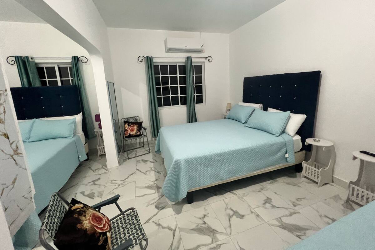 Un dormitorio con cama, una silla, una mesita y una ventana con cortinas.