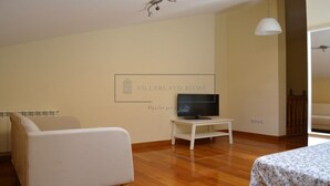 A room with a flat-screen TV on a white stand, a white sofa, and a bed with a floral bedspread. - VILLARCAYO HOME  3-habitaciones, lujoso apartamento muy amplio y céntrico (VILLARCAYO)