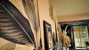 Un pasillo con un cuadro abstracto de gran tamaño, un retrato enmarco y un jarrón decorativo con plantas secas.