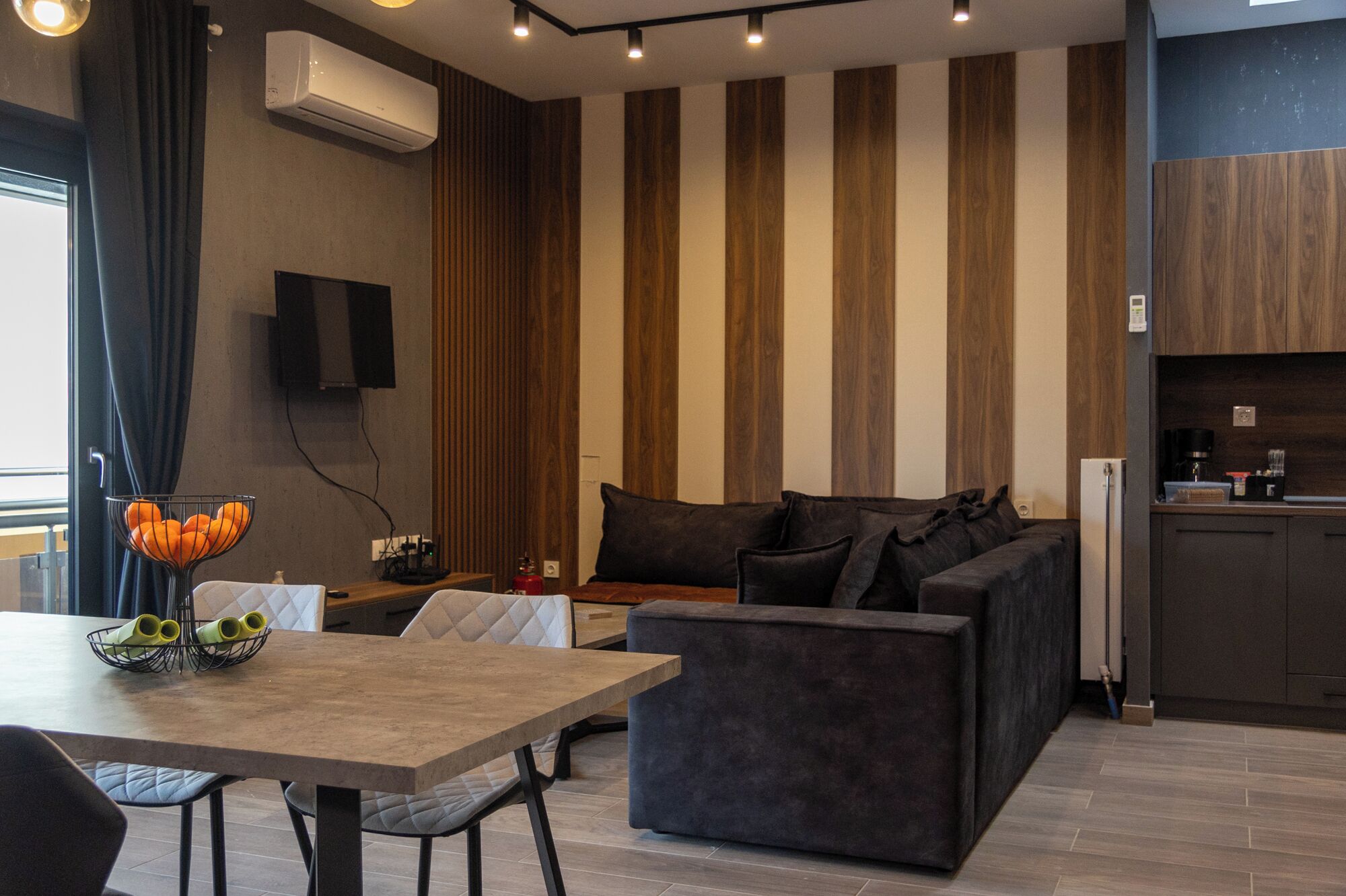 A modern living room with a sofa, a dining table with chairs, and a kitchen area with a countertop and cabinets.