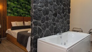 Un baño moderno con una pared de acento de piedra, una bañera blanca y una cama con cabecera y almohadas.
