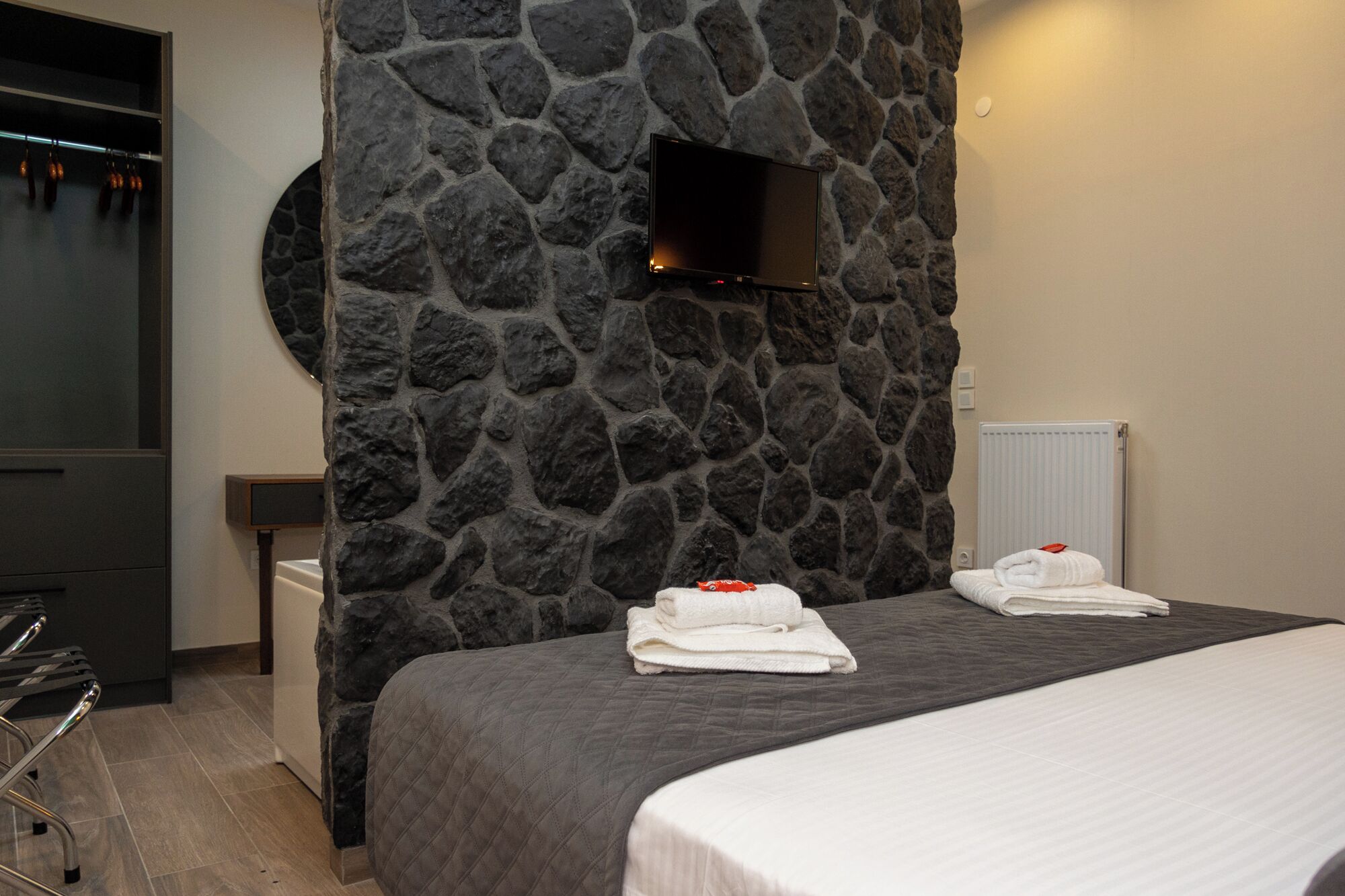 Hotelkamer met een stenen muur, een flatscreen televisie, een bed met een grijze sprei en twee handdoeken op het bed.