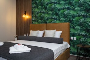 Une chambre d’hôtel avec un lit, une table de chevet, une lampe fixée au mur et un papier peint aux motifs tropicaux.
