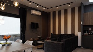 Una sala moderna con un sofá, una mesa de comedor con sillas, un televisor y una zona de cocina con un refrigerador.