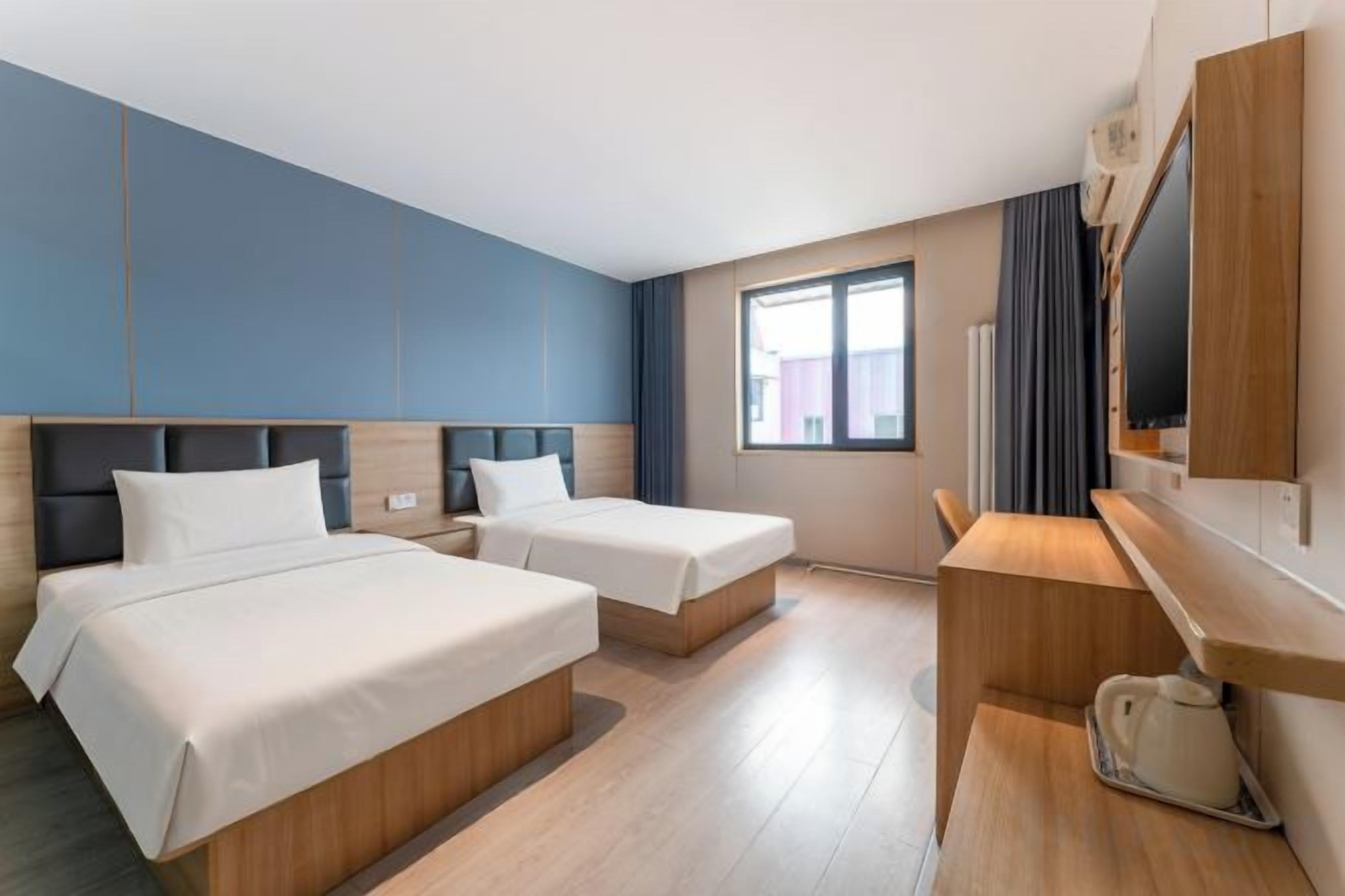 A hotel room with two beds, a desk, and a television.