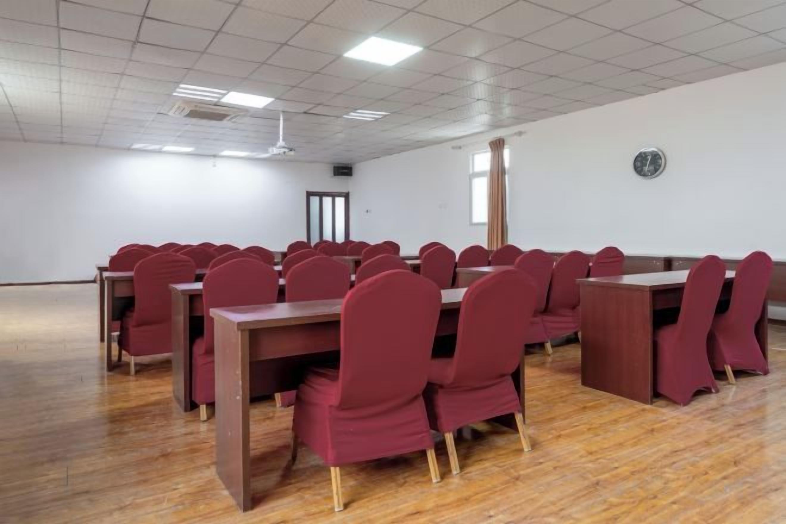 A conference room with multiple tables and chairs, a wooden floor, and a white ceiling with recessed lighting.