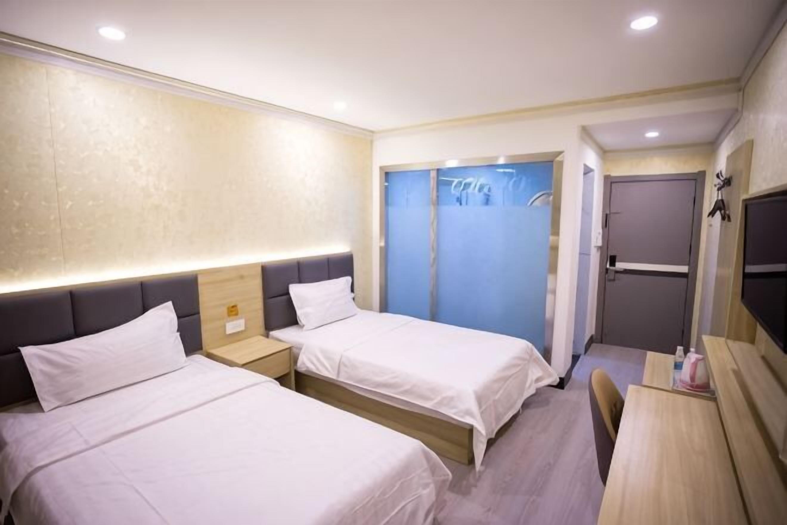 A hotel room with two beds, a desk, a chair, a TV, and a shower area.