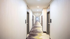 A long, narrow hotel corridor with a carpeted floor, doors on both sides, and a ceiling light. - Huayi Hotel(Tianjin Dongli Development Zone National Convention and Exhibition Center Store) (Tianjin)