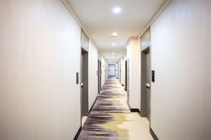 A long, narrow hotel corridor with a carpeted floor, doors on both sides, and a ceiling light. - Huayi Hotel(Tianjin Dongli Development Zone National Convention and Exhibition Center Store) (Tianjin)