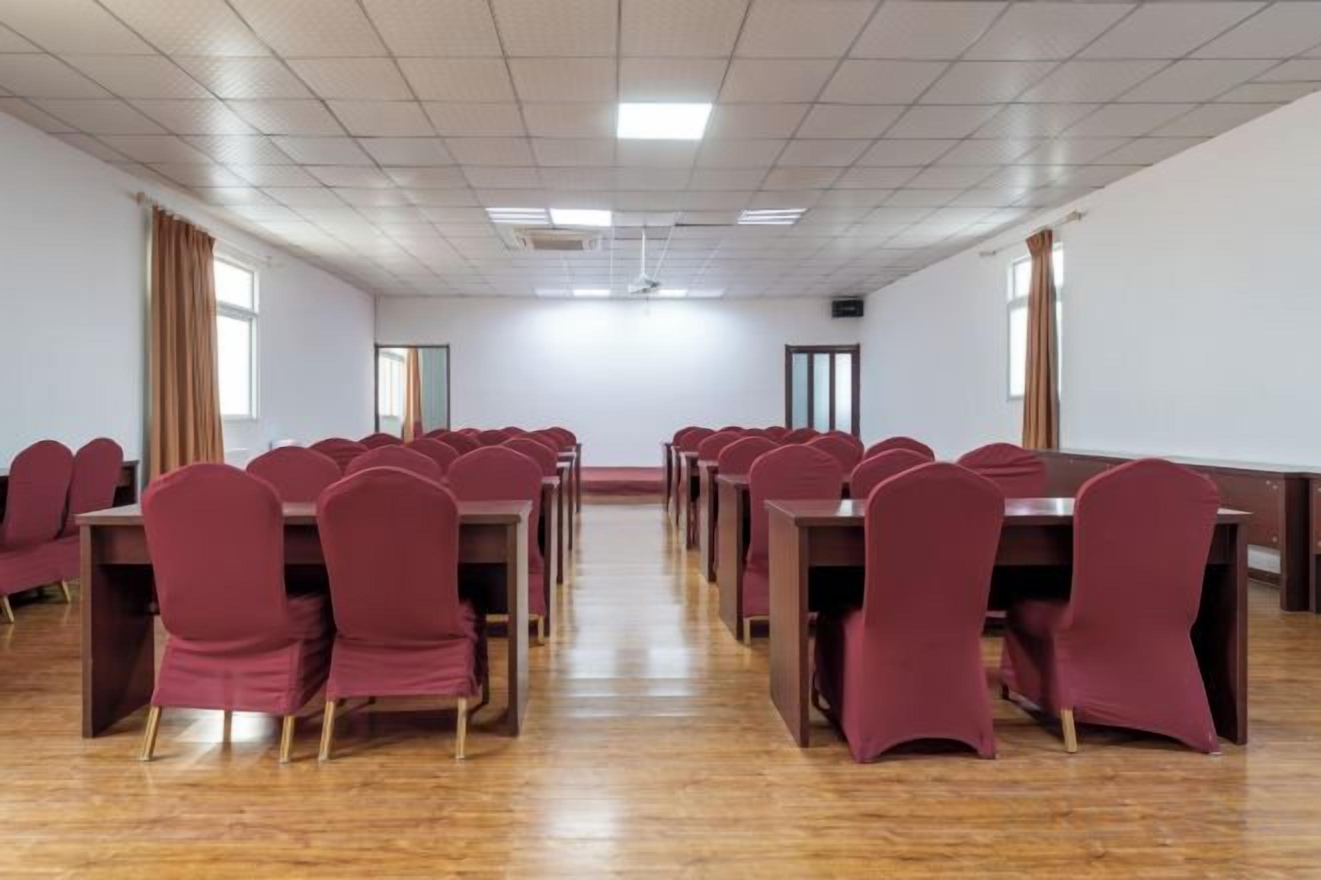 Sala de conferência com mesas e cadeiras dispostas em fileiras, um quadro branco e uma tela de projeção.