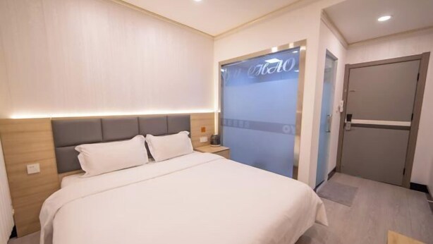 A hotel room with a bed, a nightstand, a wall-mounted TV, and a door. - Huayi Hotel(Tianjin Dongli Development Zone National Convention and Exhibition Center Store) (Tianjin)
