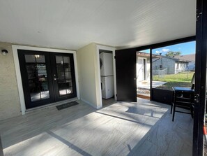 Un'ampia area patio con una porta scorrevole che dà su un giardino, una porta nera e un piccolo angolo salotto.