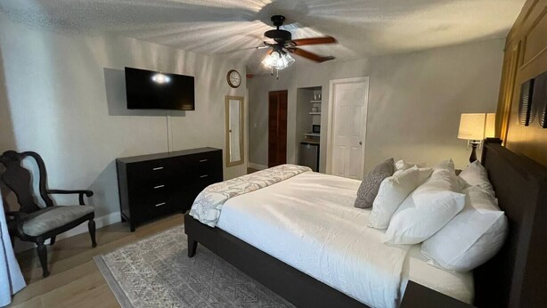 Ein Schlafzimmer mit einem Bett, einem Fernseher, einem Deckenventilator, einem Schminktisch, einem Stuhl und einem Kleiderschrank.