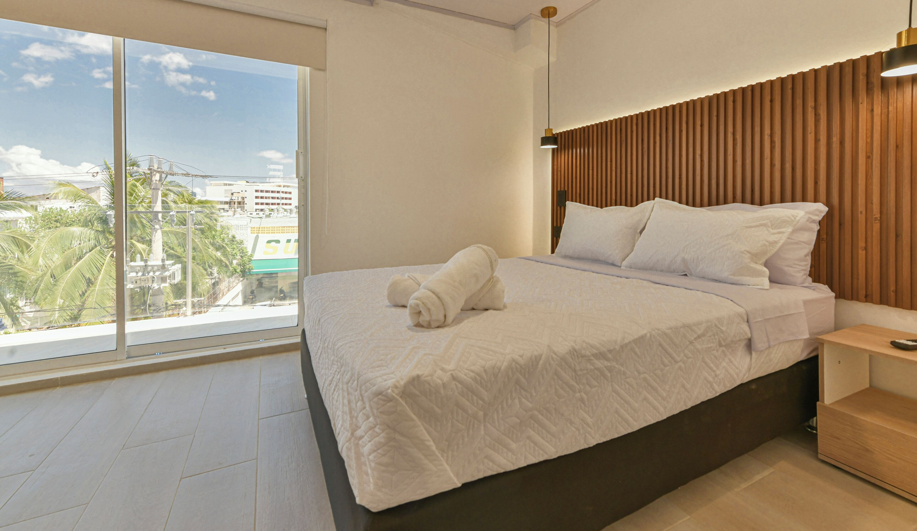 A modern hotel room with a large window, a neatly made bed, and a wooden headboard.