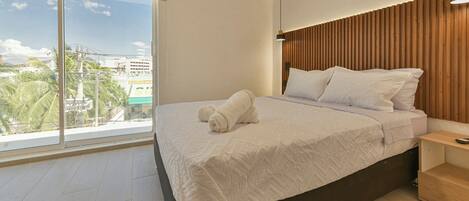 A modern hotel room with a large window, a neatly made bed, and a wooden headboard.