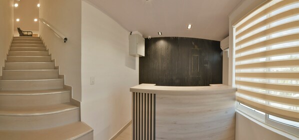 A modern interior with a curved reception desk, a staircase, and a window with blinds. - Hotel Blu Sai (San Andres)