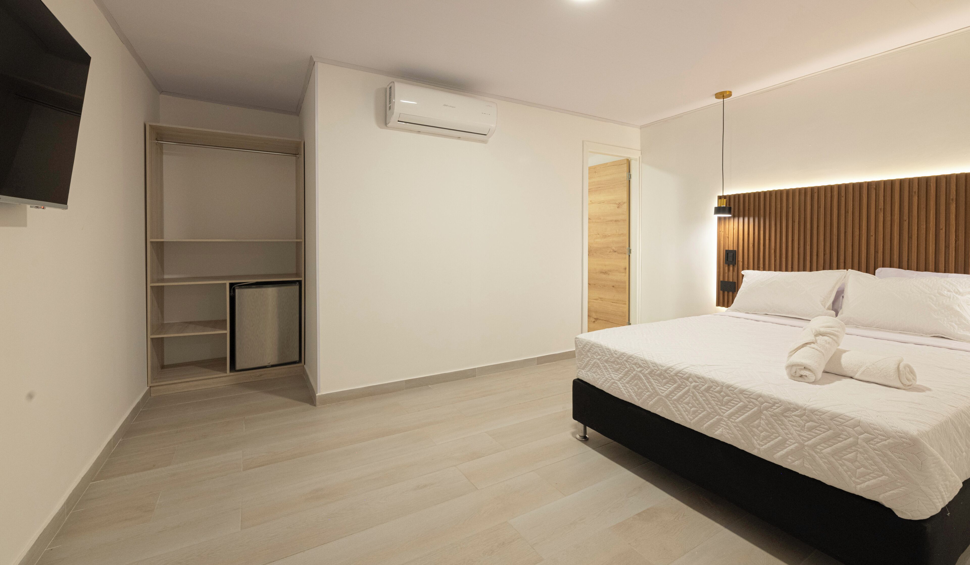 A bedroom with a bed, a wardrobe, a built-in air conditioner, and a small refrigerator.