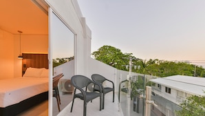 A balcony with a bed and two chairs, overlooking a building and trees. - Hotel Blu Sai (San Andres)