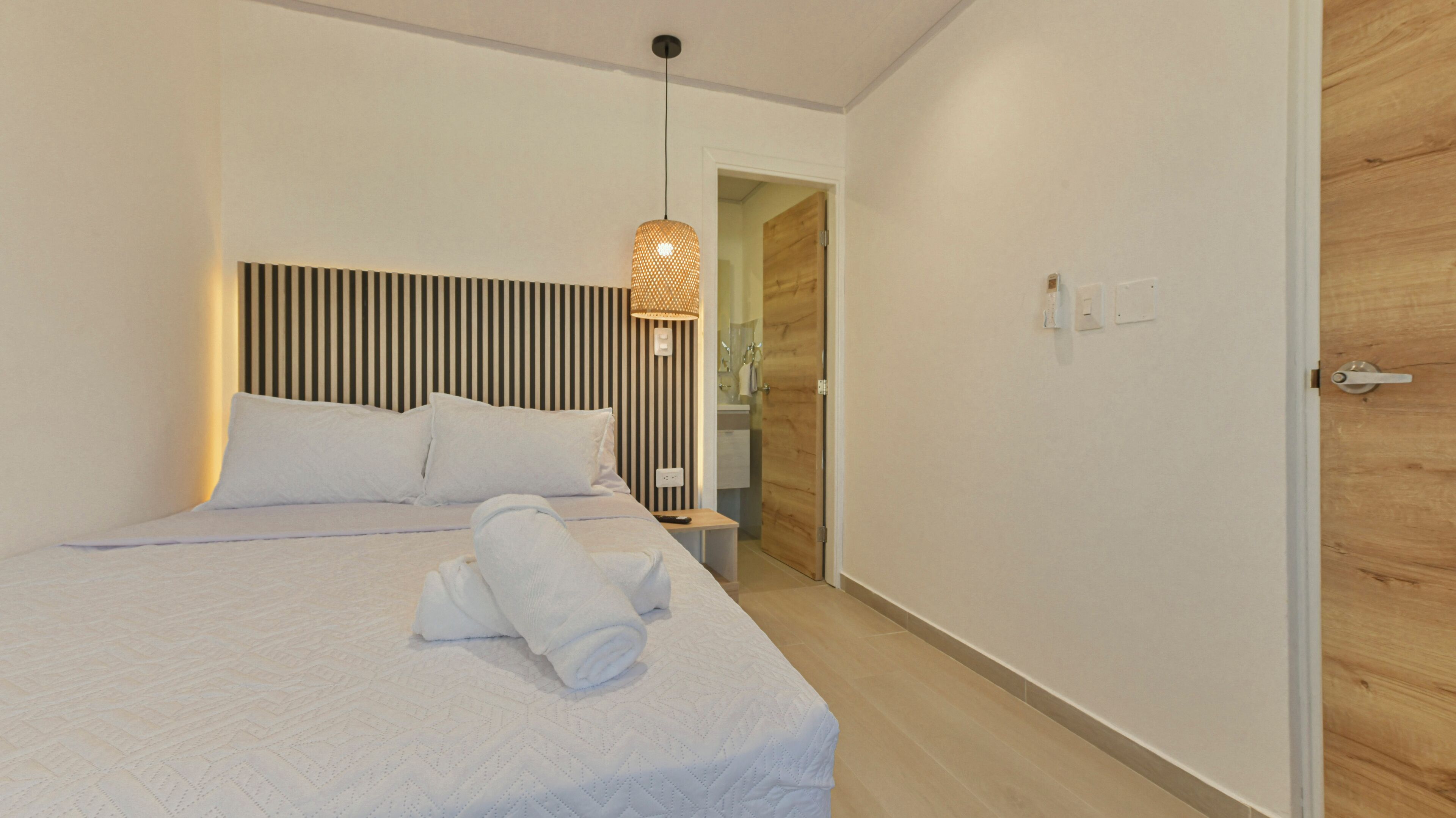 Una habitación de hotel moderna con una cama grande, una mesita de noche, una lámpara colgante y una puerta de madera.