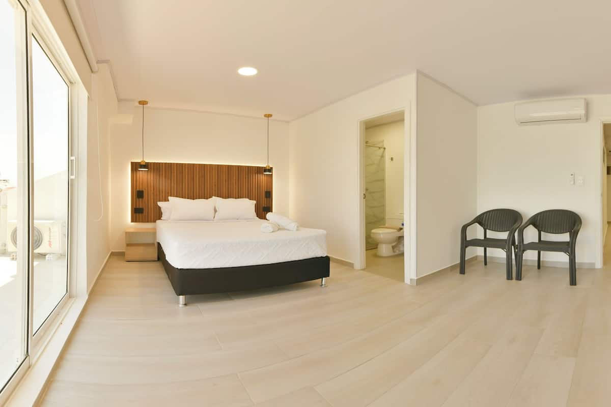 A modern bedroom with a large bed, a wooden headboard, a bedside table, and a chair.