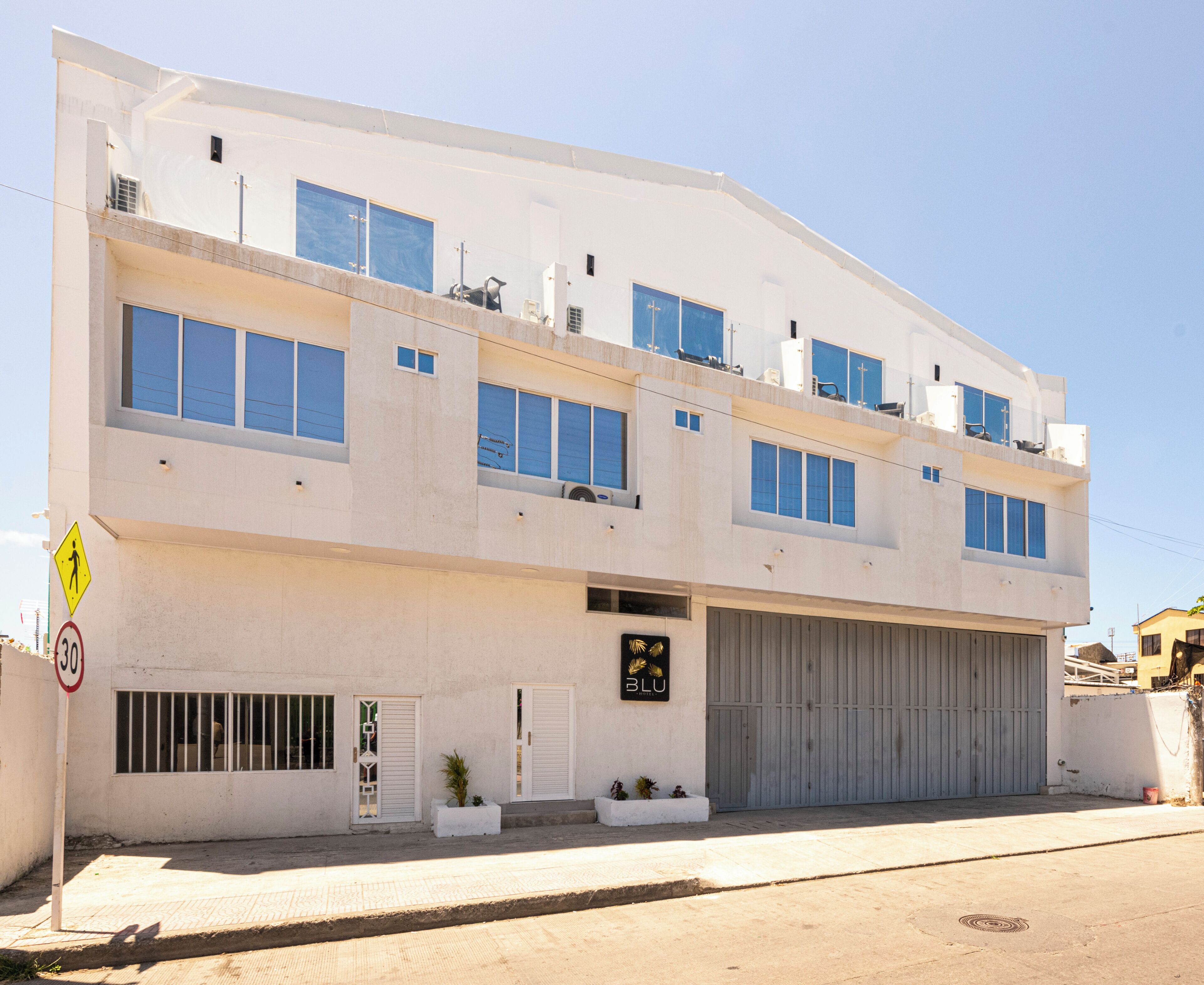 A multi-story building with a large garage door, a pedestrian crossing sign, and a speed limit sign.