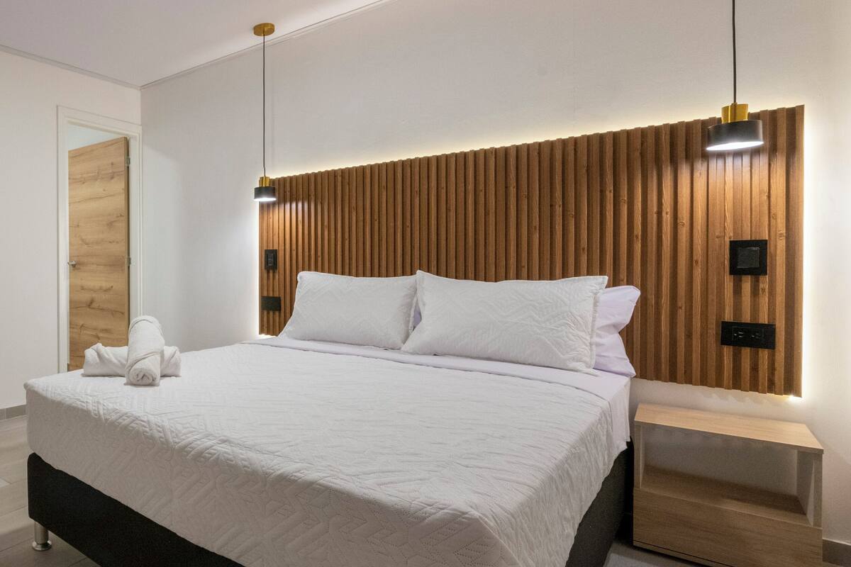 A modern bedroom with a wooden headboard, a neatly made bed with white linens, and bedside tables with lamps.