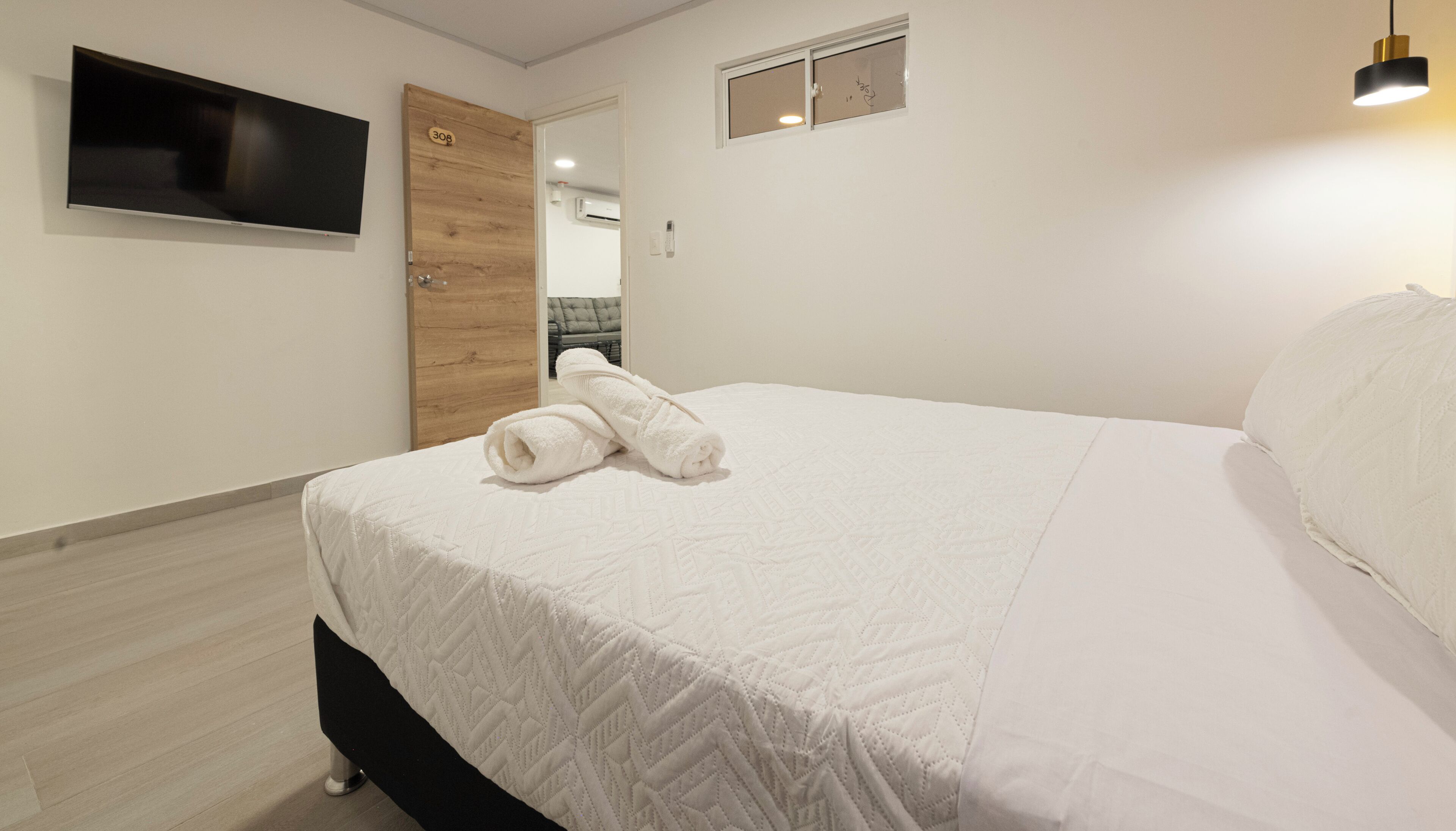 A hotel room with a bed, a TV mounted on the wall, a wooden door, and a small window.
