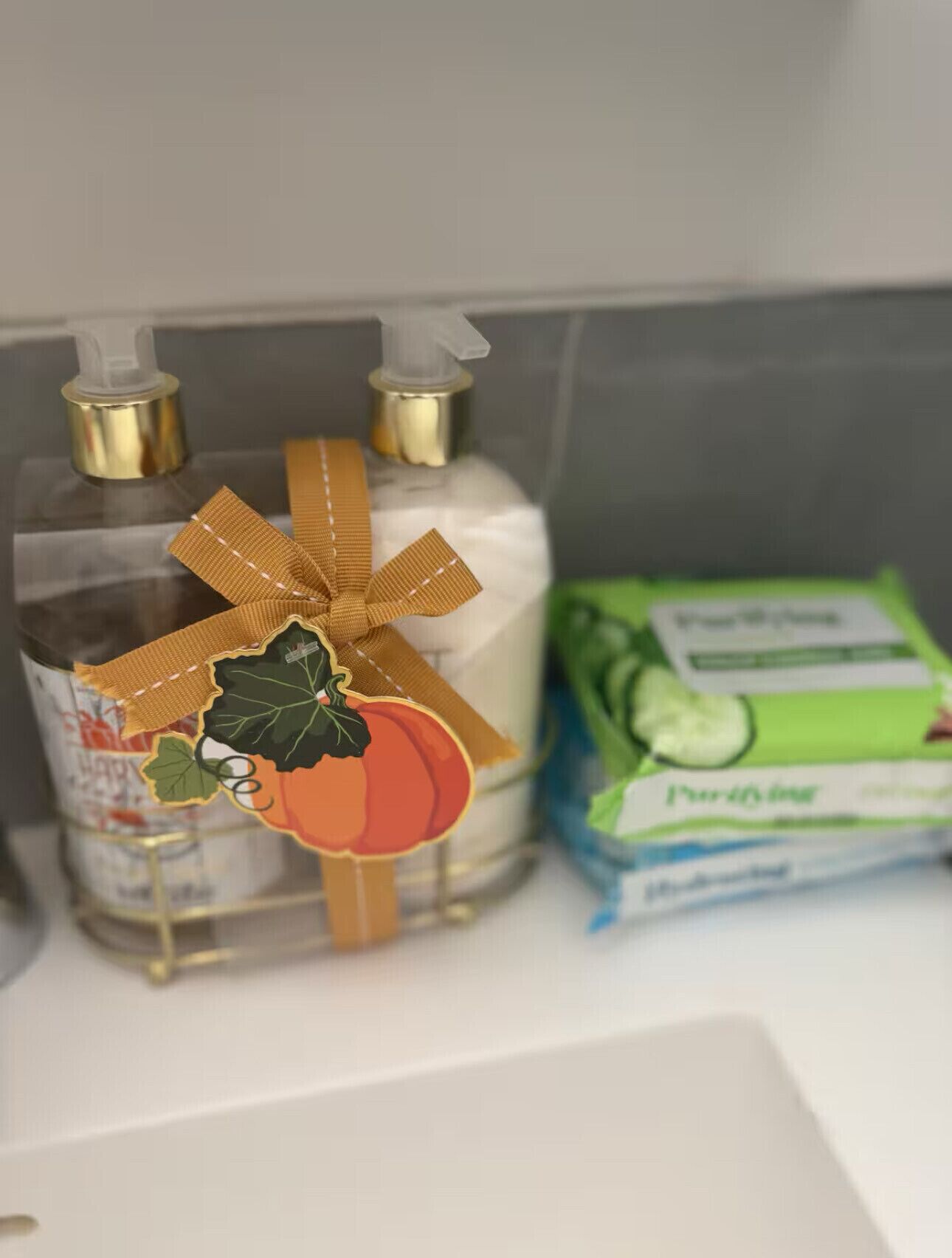 A bathroom shelf with a clear glass bottle of liquid soap, a bar of soap, and a package of lotion.