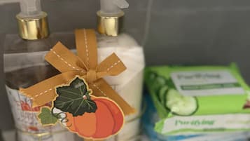 Un estante de baño con una botella de vidrio transparente de jabón líquido, una pastilla de jabón y un paquete de loción.