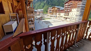 Een houten balkon met uitzicht op een bergresort, inclusief gebouwen en een heldere lucht.