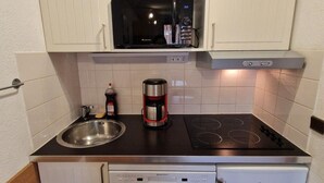 Een kleine keuken met een magnetron, koffiezetapparaat, gasfornuis en vaatwasser.