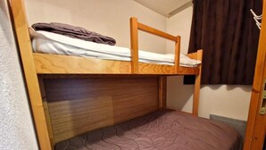 Een stapelbed met houten frame, een onderbed met paars dekbed en een bruin gordijn aan de rechterkant.