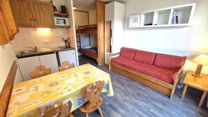 Et lille værelse med spisebord, stole, en rød sofa, køjeseng og en mikrobølgeovn.