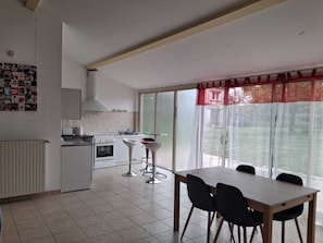 A modern kitchen with a dining area, a large window with a view, and a red curtain.