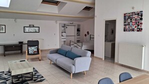 A modern living room with a sofa, a desk, and a chair. There is a kitchen area visible in the background. - Tranquil House with large pool, set in beautiful private garden. separate Gite (Paizay-le-Chapt)