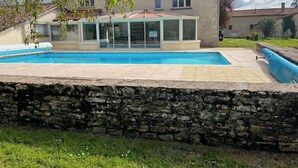 A stone wall, a swimming pool, and a house with a tiled roof. - Tranquil House with large pool, set in beautiful private garden. separate Gite (Paizay-le-Chapt)
