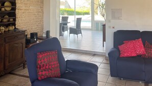 A living room with a stone wall, wooden beams, a fireplace, and a view to an outdoor patio. - Tranquil House with large pool, set in beautiful private garden. separate Gite (Paizay-le-Chapt)