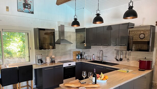 A modern kitchen with dark cabinets, a large island, and a view of greenery outside. - Tranquil House with large pool, set in beautiful private garden. separate Gite (Paizay-le-Chapt)