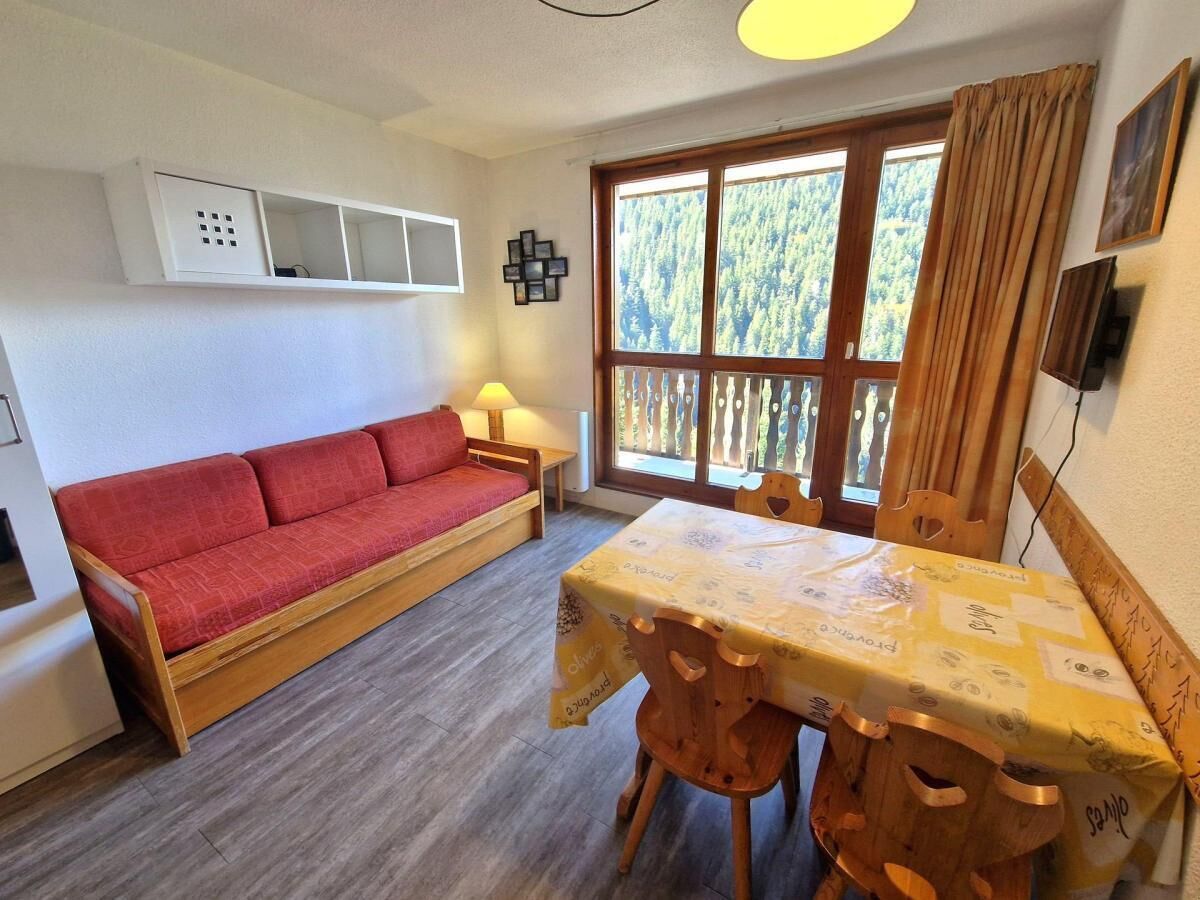 Ein Zimmer mit einer Holzdirekt, einem Tisch mit Tischdecke, einem Fenster mit Blick auf Bäume und einem Wandheizkörper.