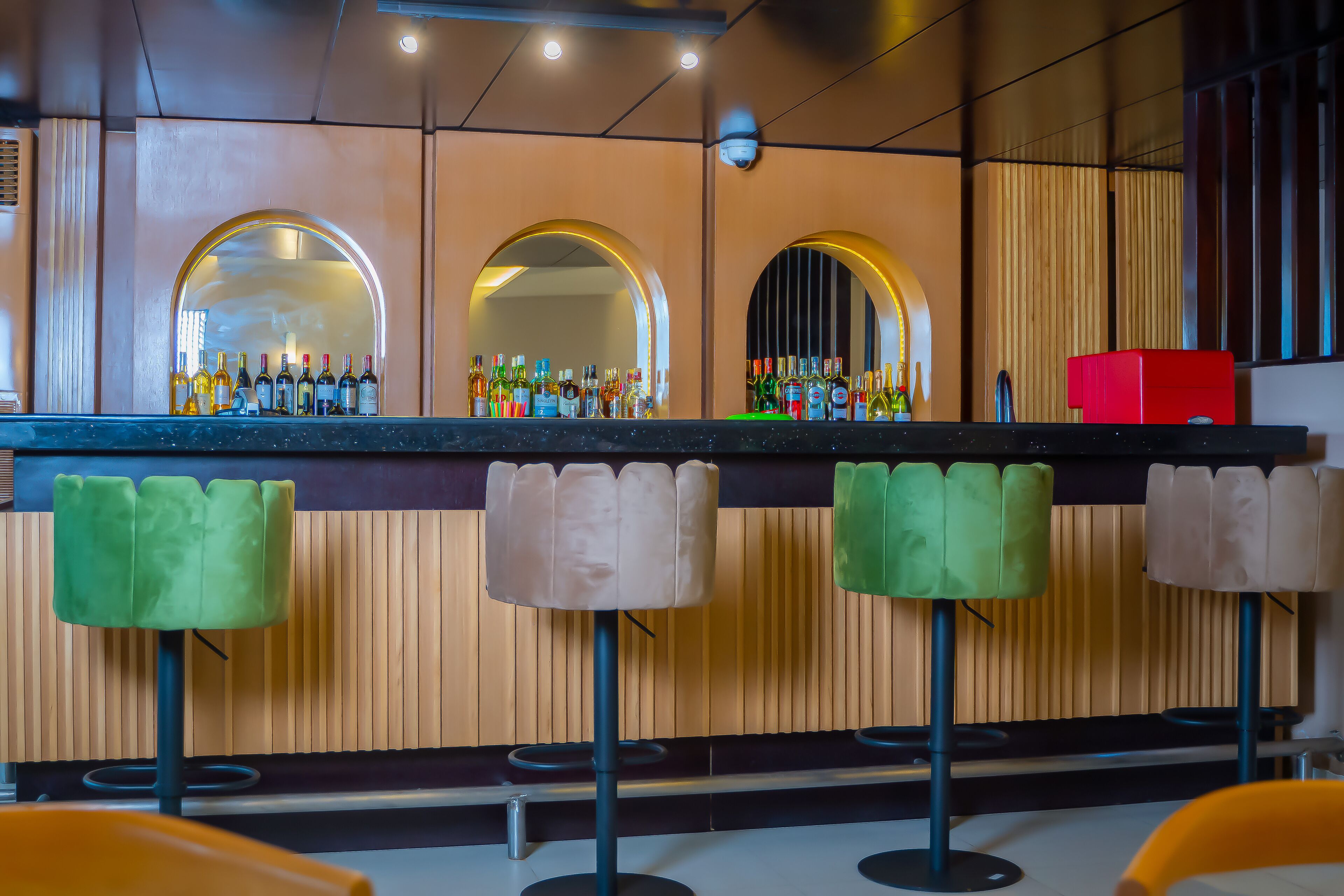 A bar area with a mirrored wall, multiple stools, and a variety of bottles on the counter.