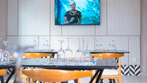 Een moderne eetruimte met houten tafels en stoelen, een flatscreen televisie aan de wand en een decoratief wandpaneel.