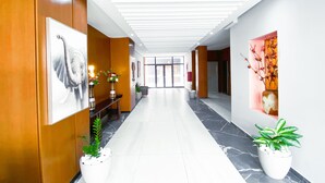 Een moderne hotellobby met een marmeren vloer, houten lambrisering en potplanten.