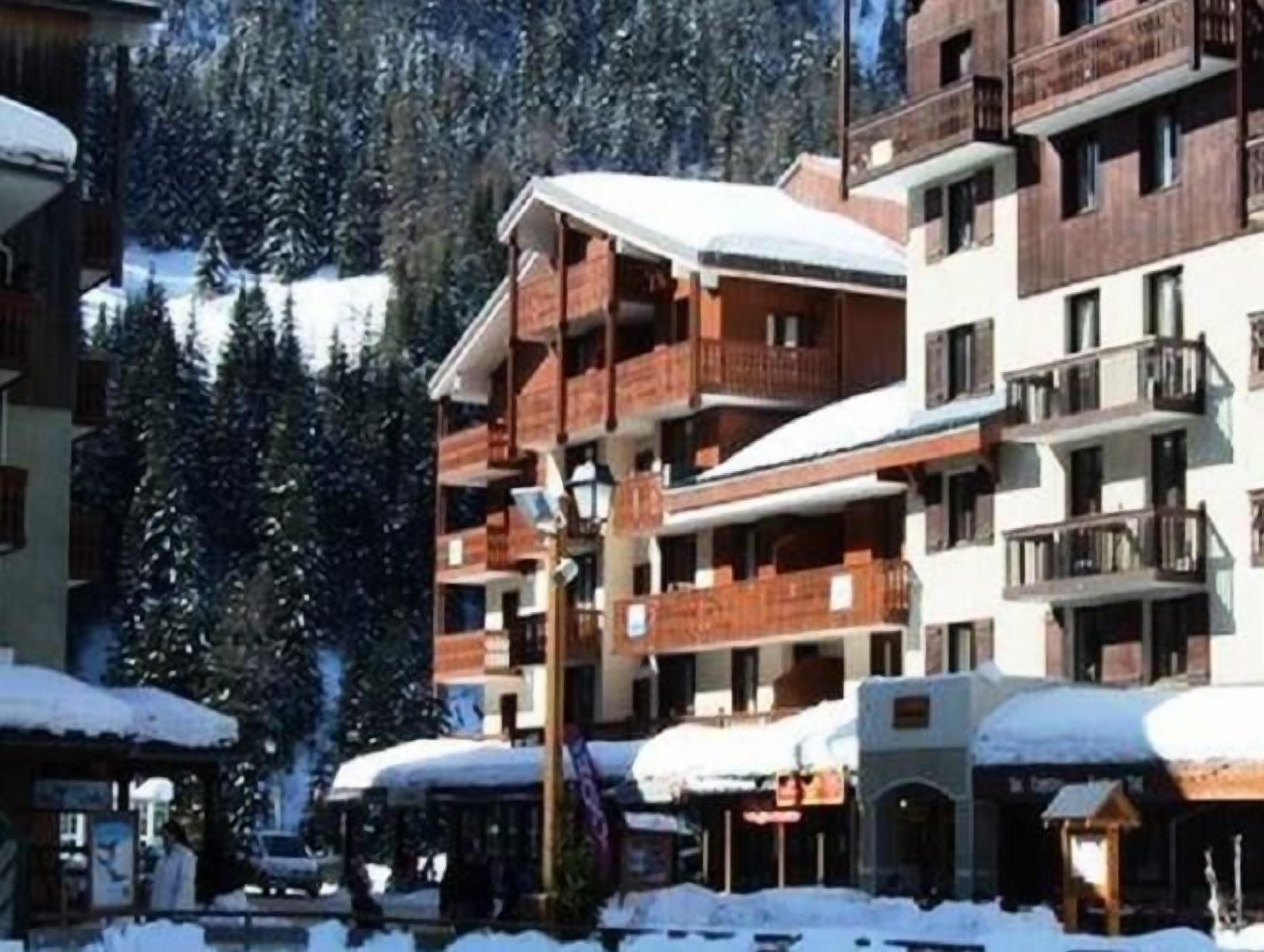 Ein mehrstöckiges Hotel mit Balkonen, umgeben von schneebedeckten Bäumen und einer Berglandschaft.