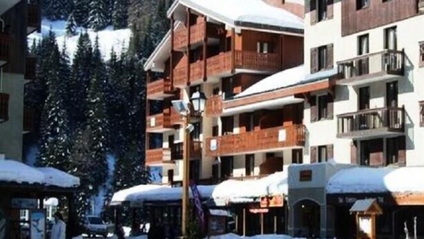 Ein mehrstöckiges Hotel mit Balkonen, umgeben von schneebedeckten Bäumen und einer Berglandschaft.