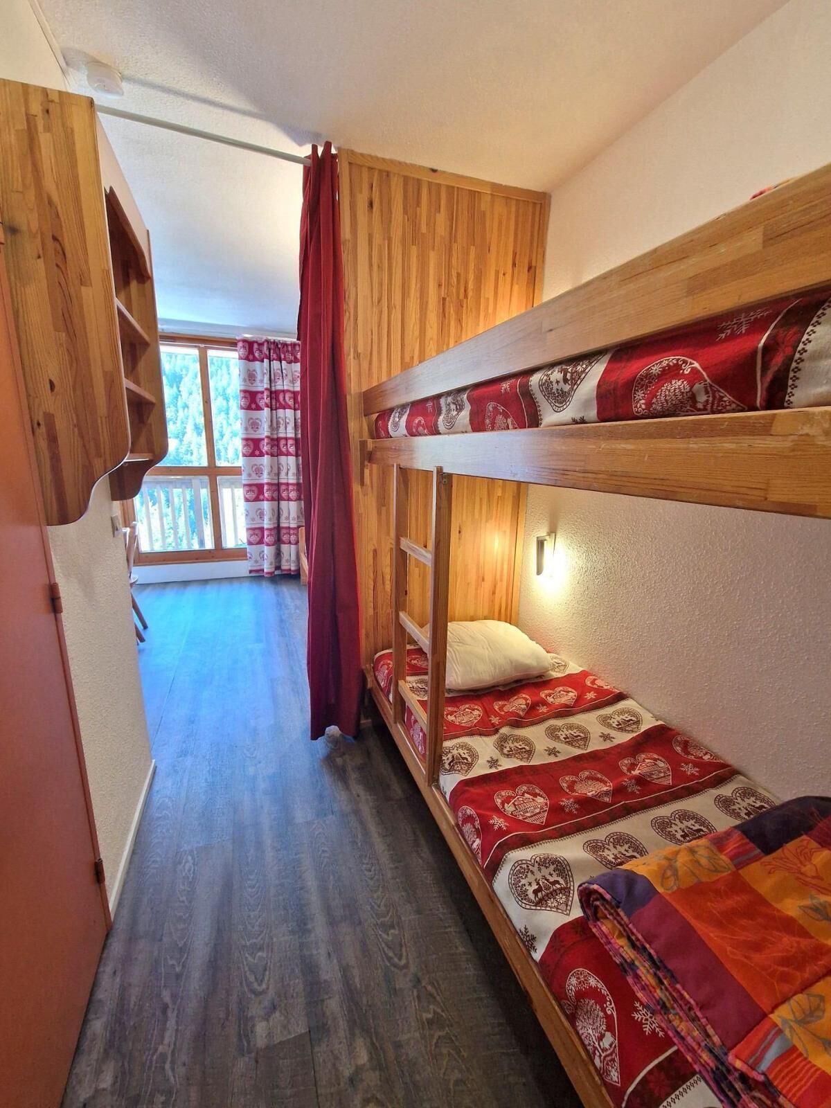 A bunk bed room with a wooden headboard, a red curtain, and a patterned bedspread.