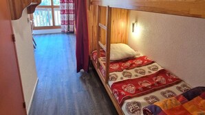 Ein Schlafraum mit Etagenbetten, einem Holzkopfteil, einem roten Vorhang und einer gemusterten Bettdecke.