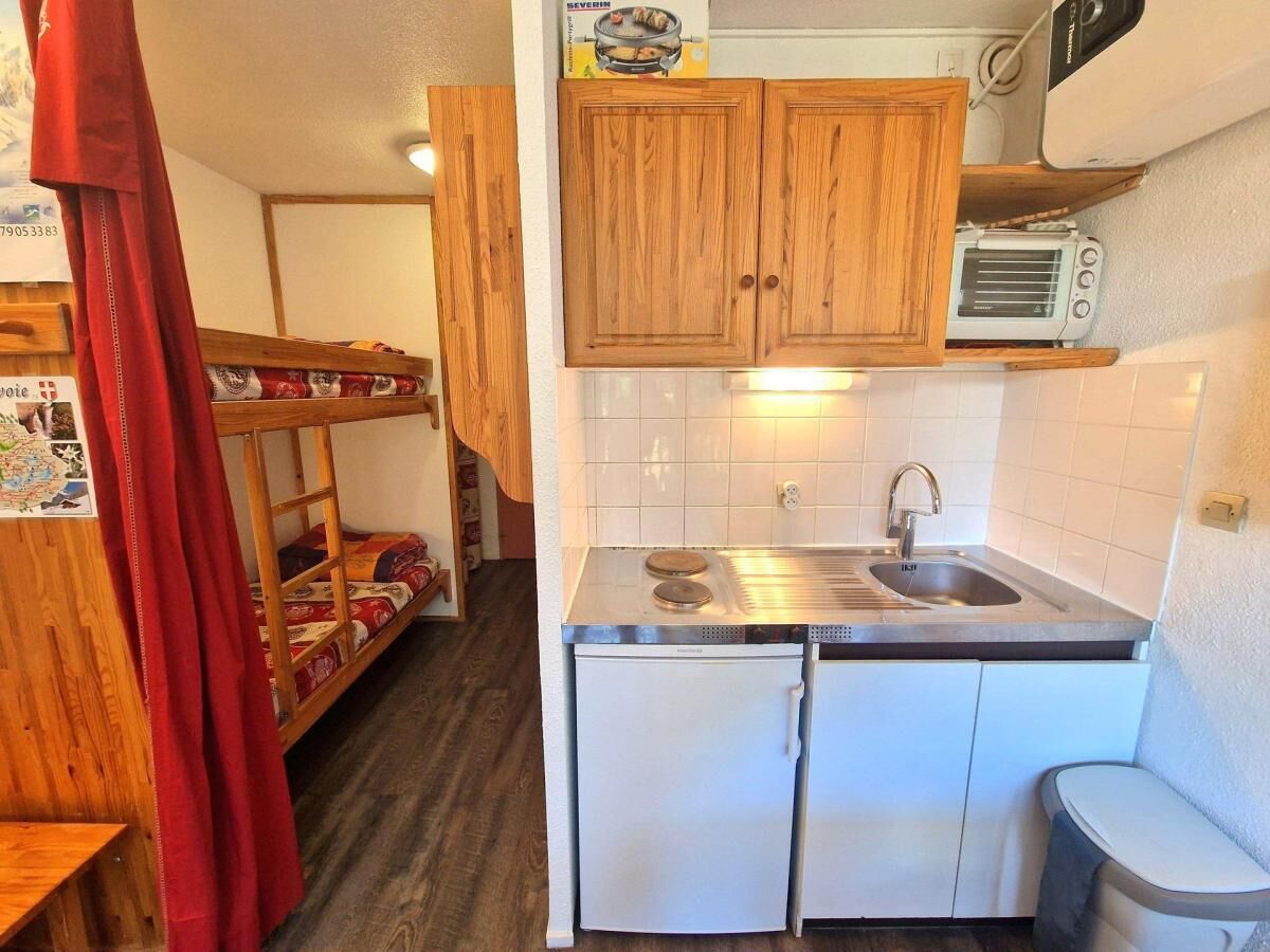 Une cuisine de taille réduite, avec des meubles de rangement en bois, un évier et un petit réfrigérateur.